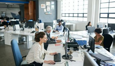 A group of coworkers are sharing a table and working on desktop computers.