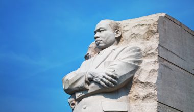 Statue of Martin Luther King Jr. with arms crossed, set against a blue sky.