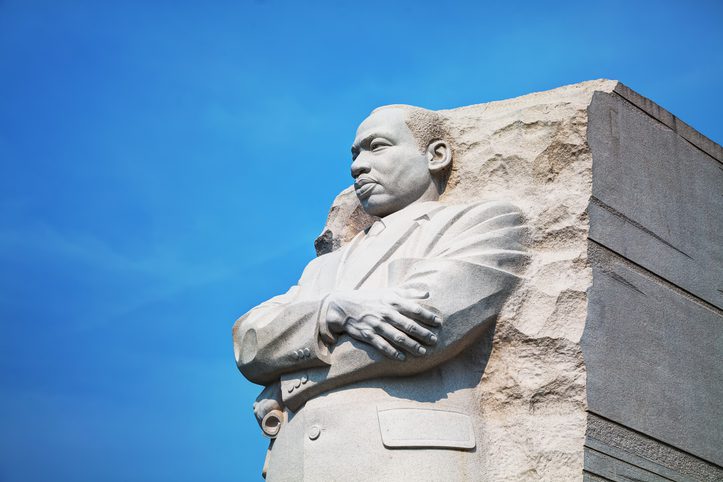 Statue of Martin Luther King Jr. with arms crossed, set against a blue sky.