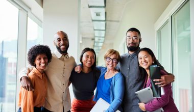 Portrait of a group of diverse businesspeople smiling while standing arm in arm together in an office corridor