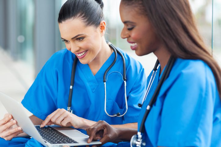 Two healthcare professionals in blue scrubs looking at a laptop.