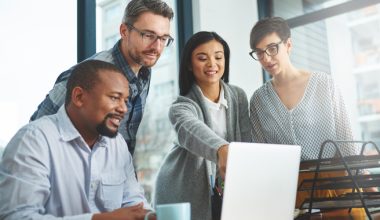 Four people gathered around a laptop in an office.