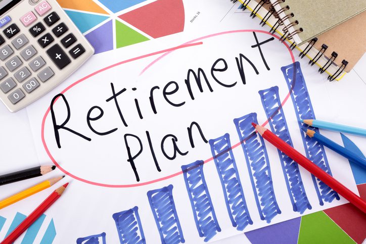 "Retirement Plan" written on a paper with blue bar graphs, surrounded by pencils and a calculator.