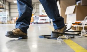 Person stepping on black strapping on a warehouse floor.