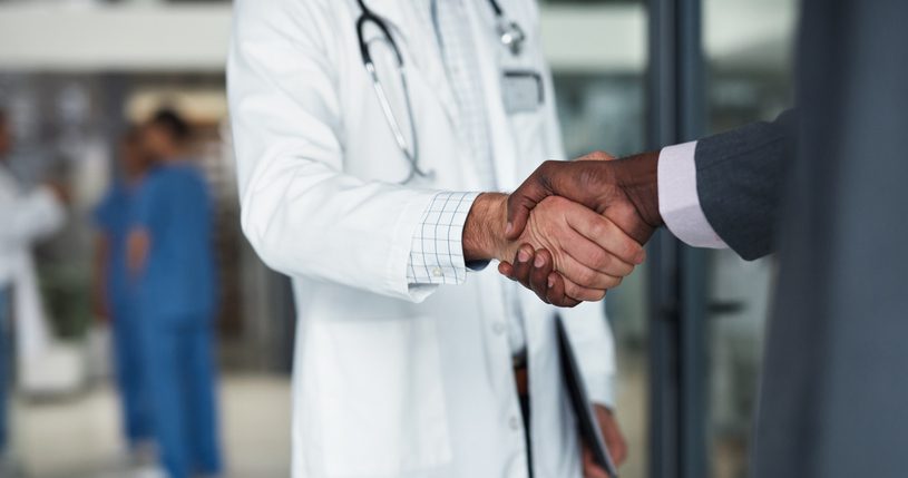 Handshake between a healthcare professional in a lab coat and a business professional, symbolizing healthcare staffing partnership and collaboration.
