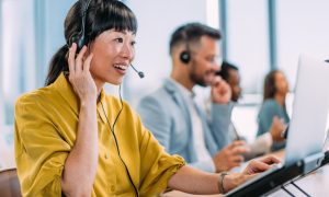 Customer service team in modern office using headsets and laptops for support calls, with natural light from large windows enhancing productivity.