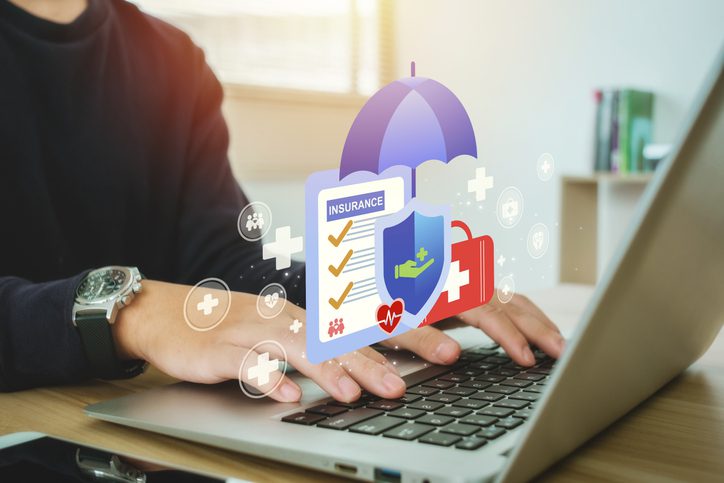 Person typing on laptop with health insurance and benefits icons including checklist, medical shield, first aid kit, and heartbeat symbols.