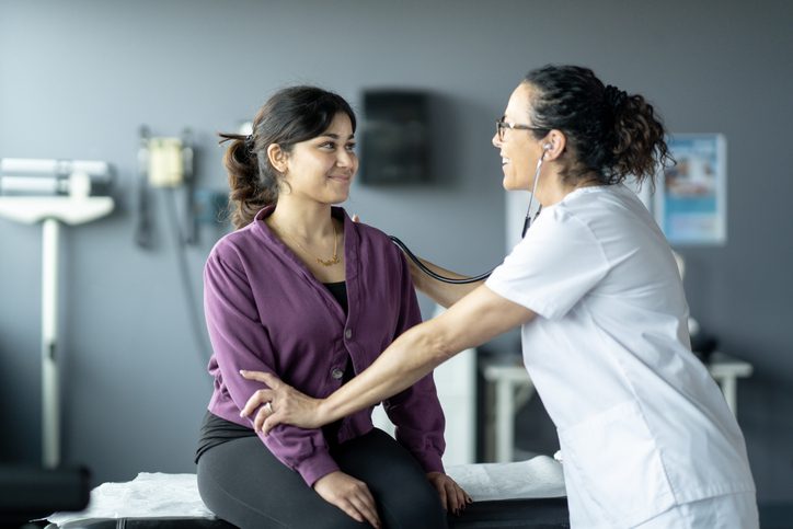 A healthcare worker next to a patient in a purple shirt.