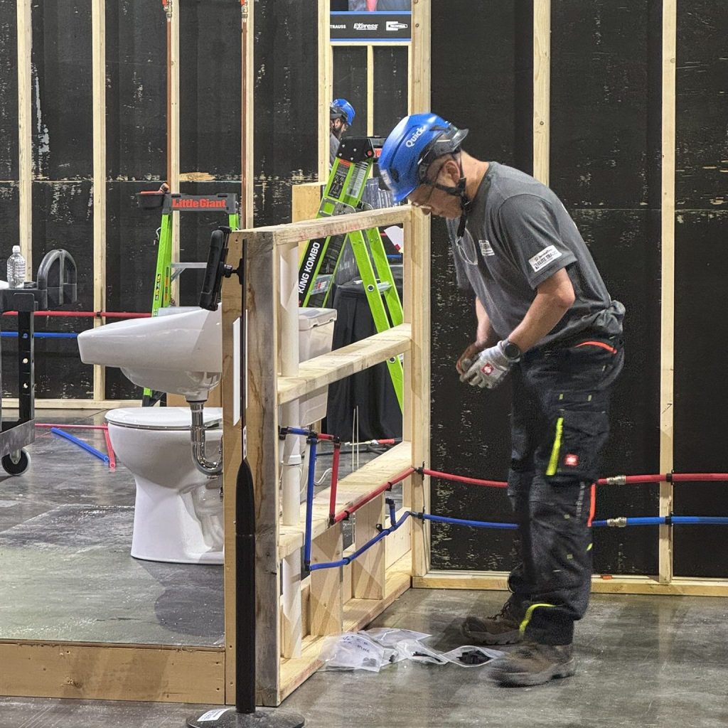Competitor working on a plumbing installation during the Elite Trades Championship Series, showcasing skilled trades expertise with pipes and fixtures.