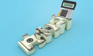 A calculator sits on top of interlocking puzzle pieces designed to look like hundred‑dollar bills against a light blue background.